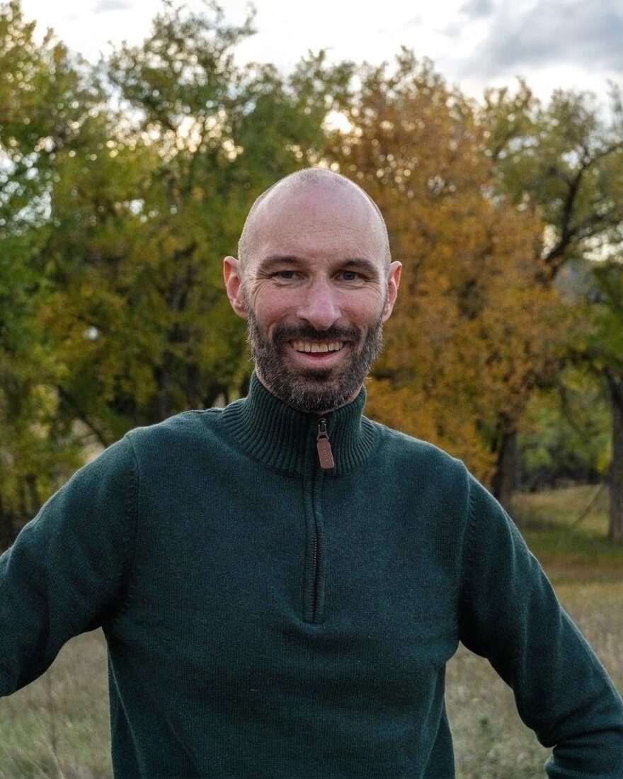 Paul Otto, smiling, in a green quarter-zip sweater, with autumn cottonwoods behind